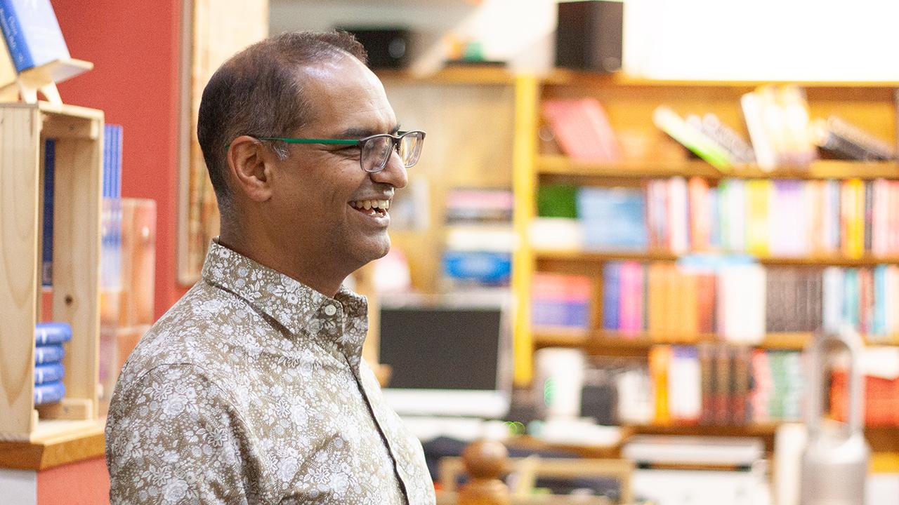 Side profile of Charan Ranganath laughing and wearing glasses with Avid Reader bookstore in background