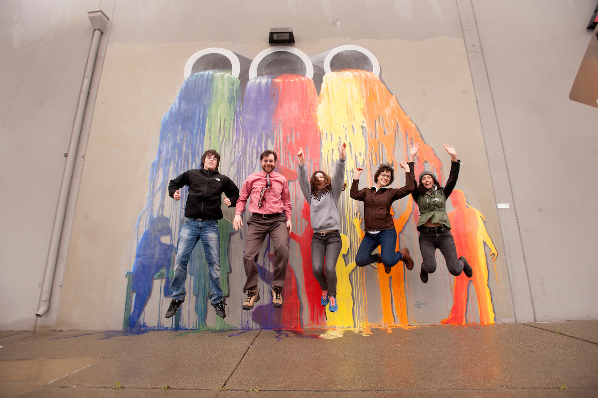 "students and instructor jump in front of art mural"