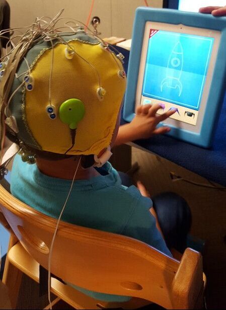 Photo of a child wearing a cap with electrodes and responding to images on a computer screen