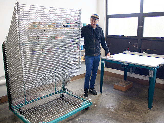 Dan Quillan, art studio printmaking and painting lab technician, stands between a new drying rack for printmaking and a vacuum table for screenprinting