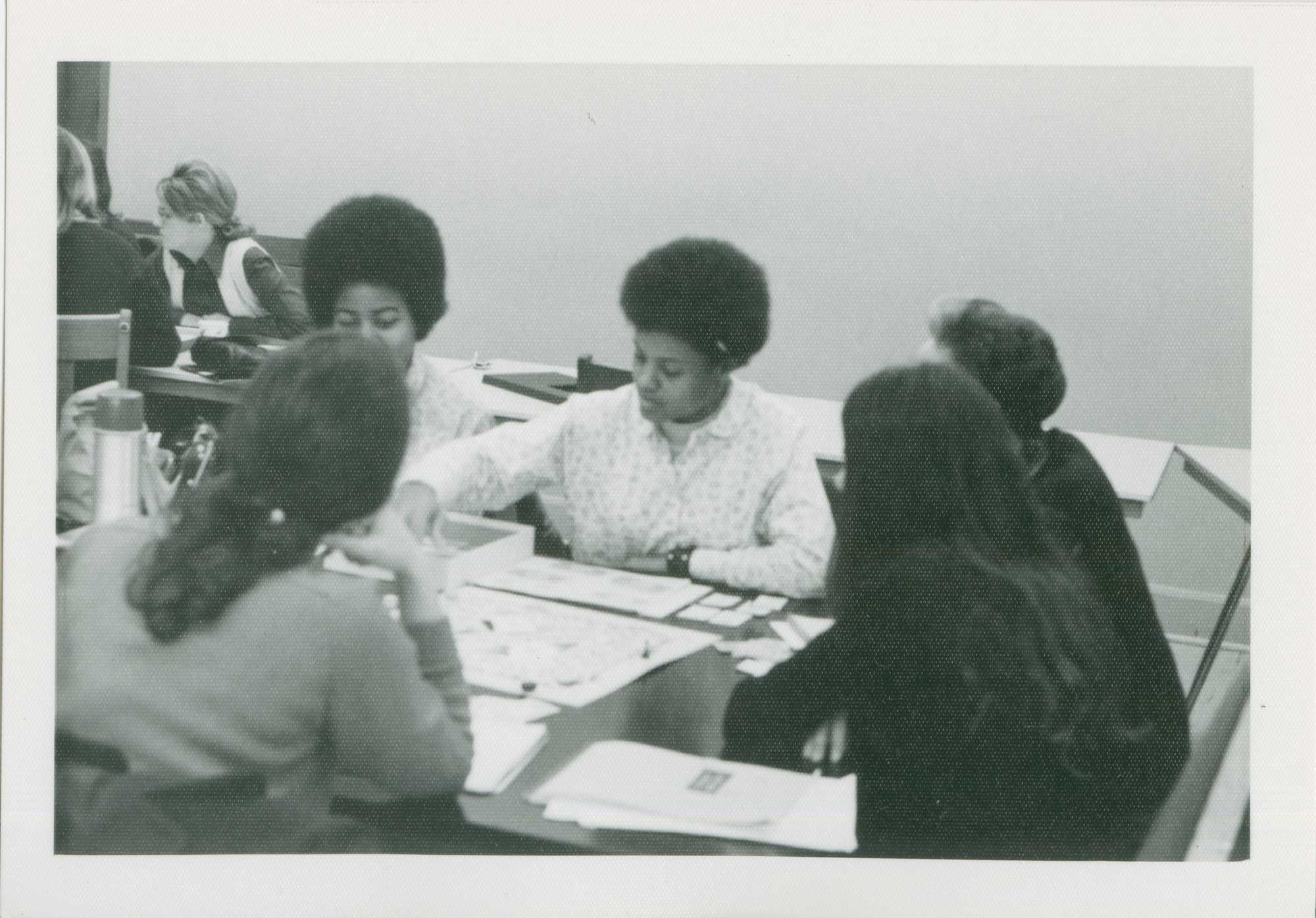 Archival photo of students, black and white, sitting at table and playing the board game. 