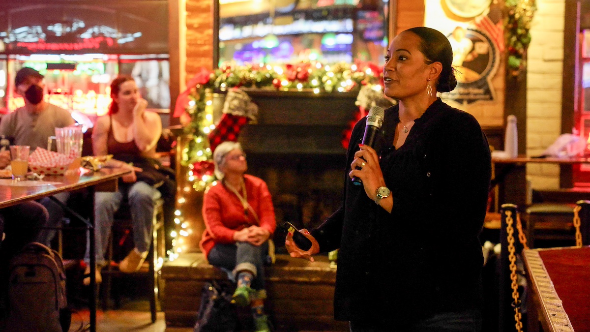 Crystal Rogers stands with a microphone in a bar as a crowd looks on. 