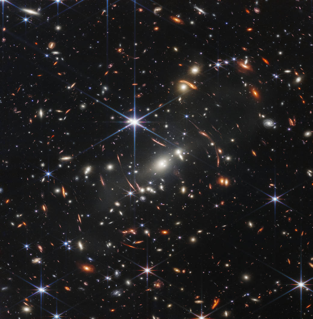 A space image showing a cluster of galaxies, some of them warped by a gravitational lensing effect. 