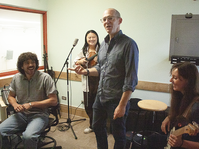 Sam Nichols, chair of the Department of Music, smiling and surrounded by three students in a new music recording studio