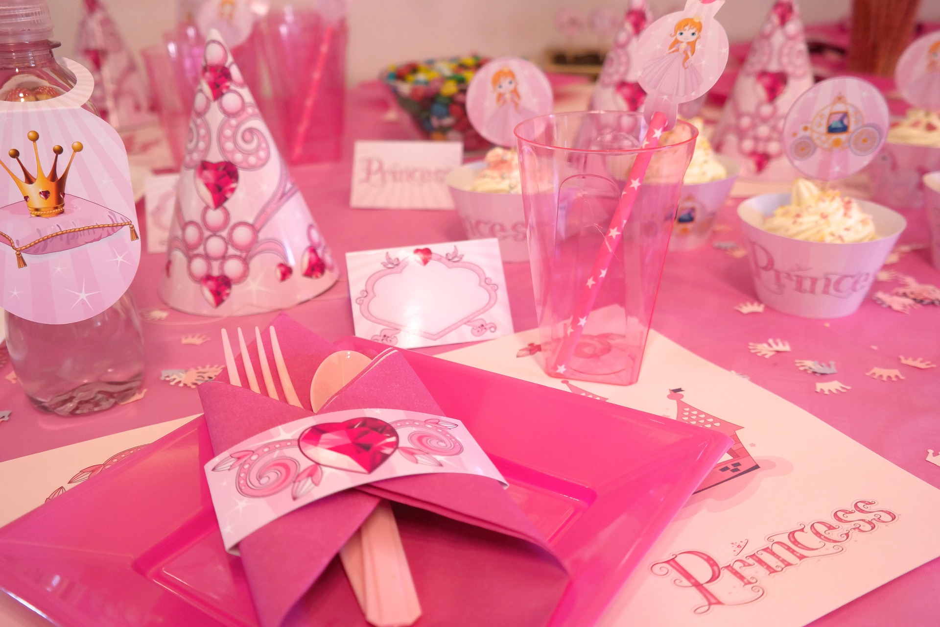 A pink table setting with pictures of princesses, crowns and jewels.