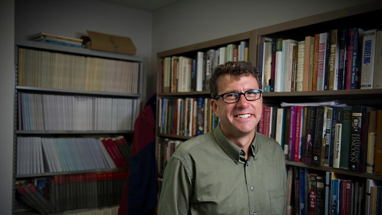Photo of historian Gregory Downs standing in front of bookshelves