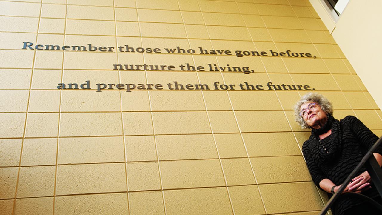 Photo: historian under sign, "Remember those who have gone before, nurture the living and prepare them for the future."