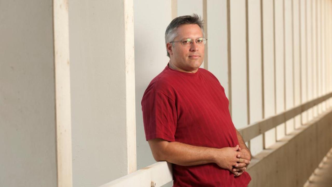 Man in red shirt and glasses leaning against side of building
