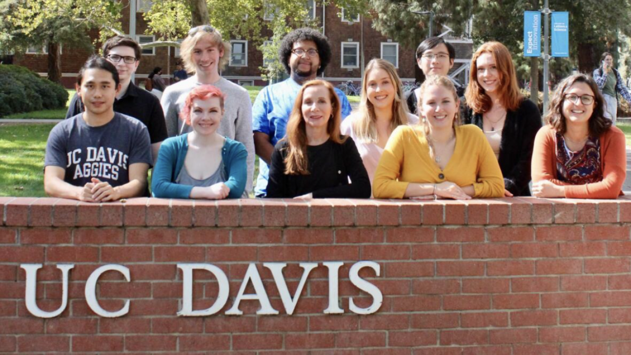 A group photo of ASPIRE students in front of a brick wall with UC Davis on the front of it.