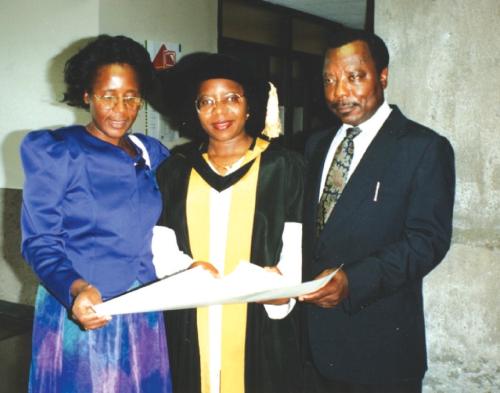 Estella Atekwana stands in the center flanked by her parents as she holds up her doctorate degree. 