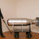 Stephen Whisler, dressed in a suit, pulls a replica of a bomb on a cart 