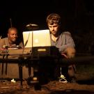 Two gorilla researchers at camp at night looking at a laptop computer