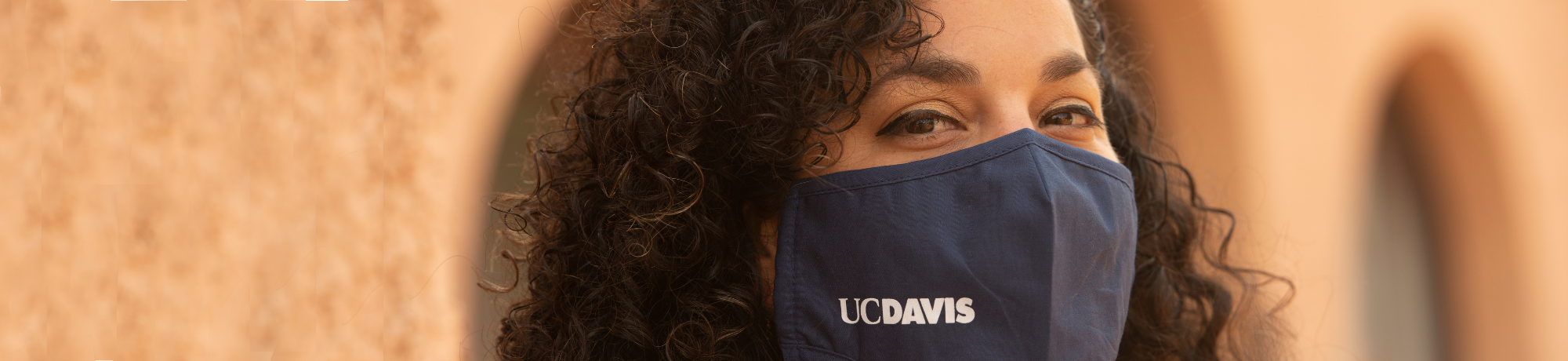 Photo of young woman wearing a face mask with UC Davis printed on it.